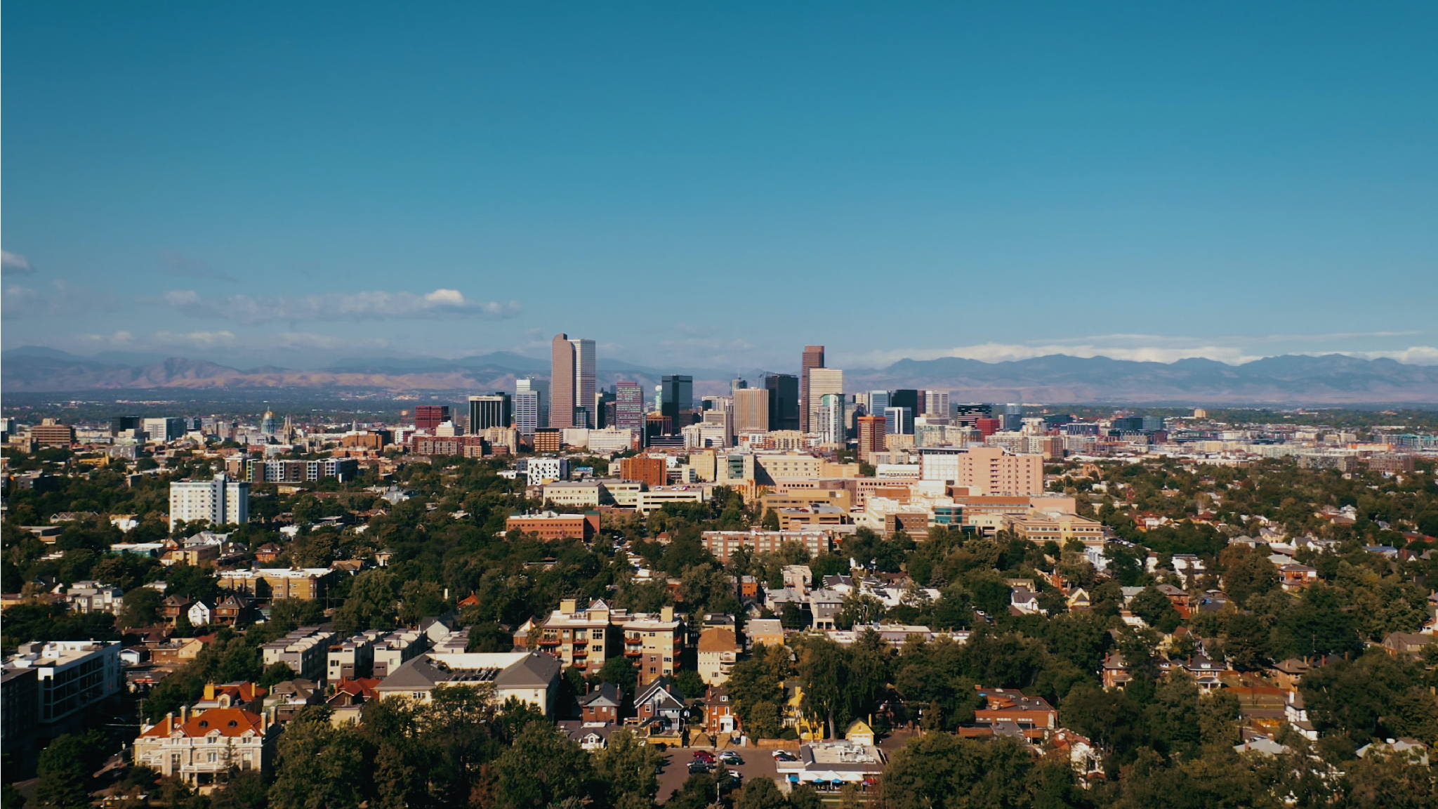 Downtown Denver skyline on a clear summer day with the Colorado Rocky Mountains in the distance.